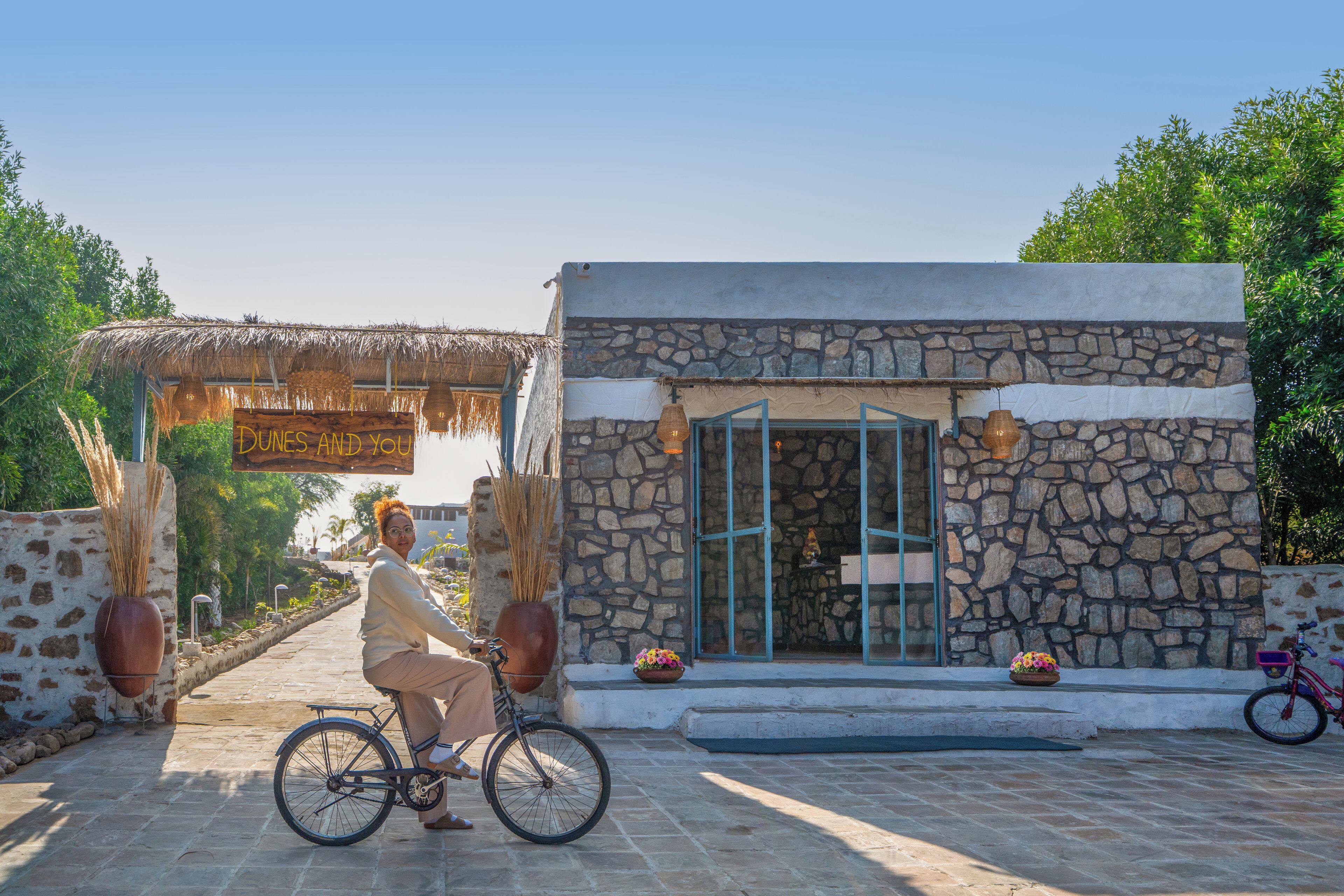 A stone building with a thatched roof entrance, a sign reading "Dunes and You," and a bicycle parked outside.