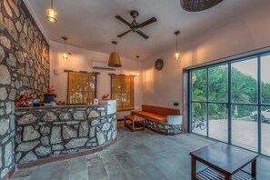 A stone wall, a wooden bench, a reception desk, and a large window with a view of greenery. - Dunes and You, Pushkar - A Luxury Pool Villas Retreat (Pushkar)
