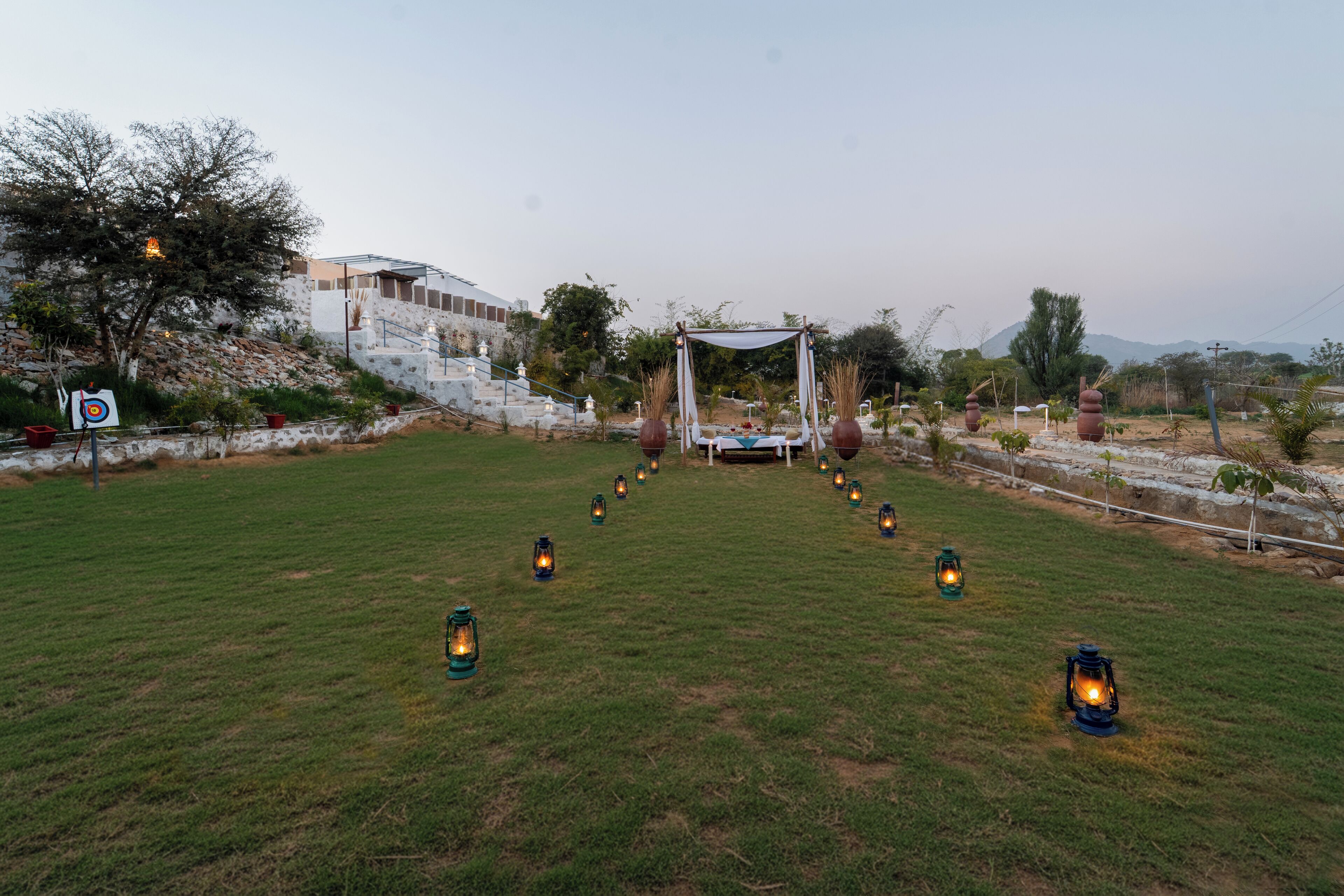 A grassy outdoor area with a canopy structure, lanterns, and a target on the left.