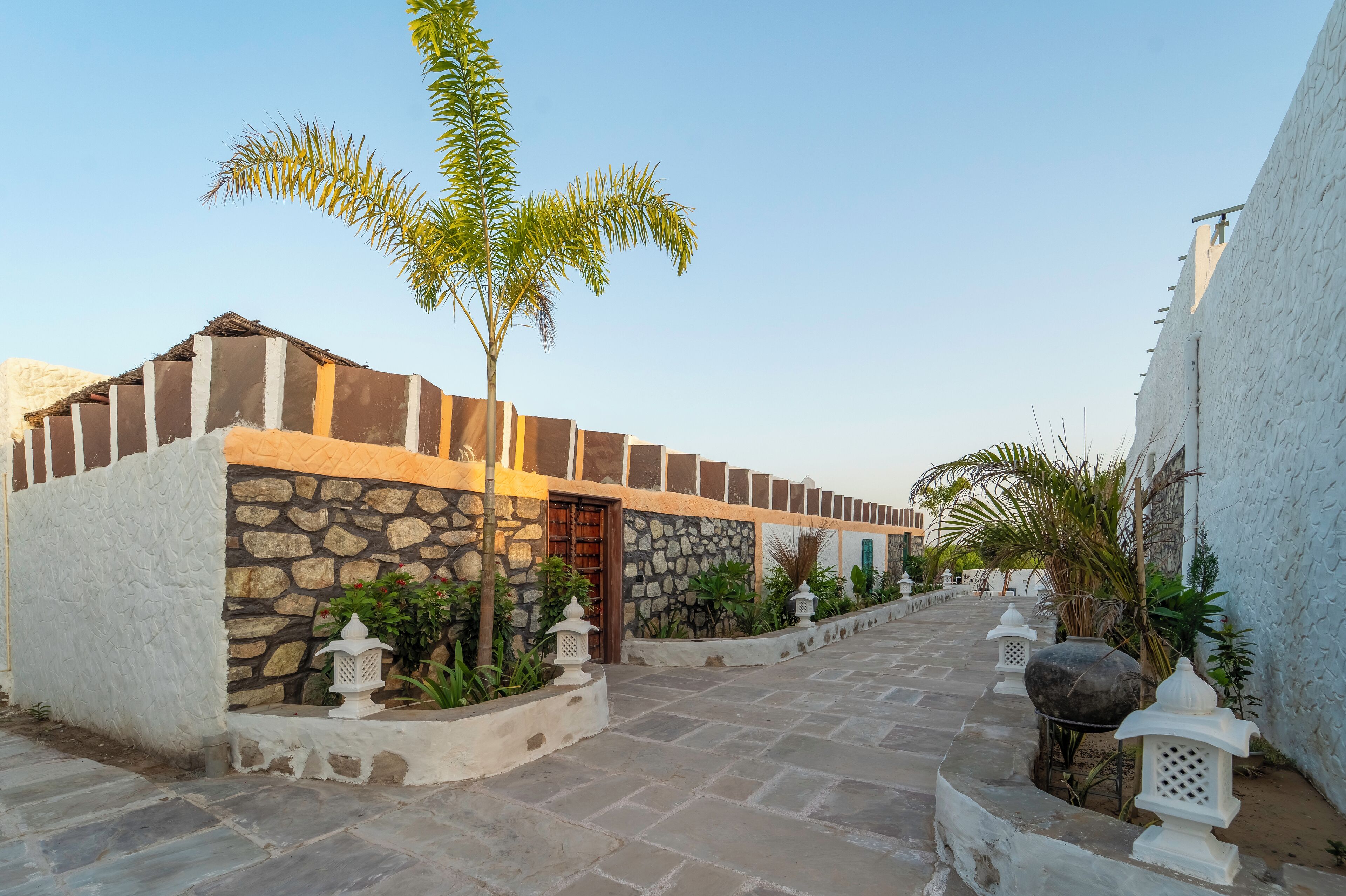 A courtyard with stone walls, a palm tree, and lanterns.
