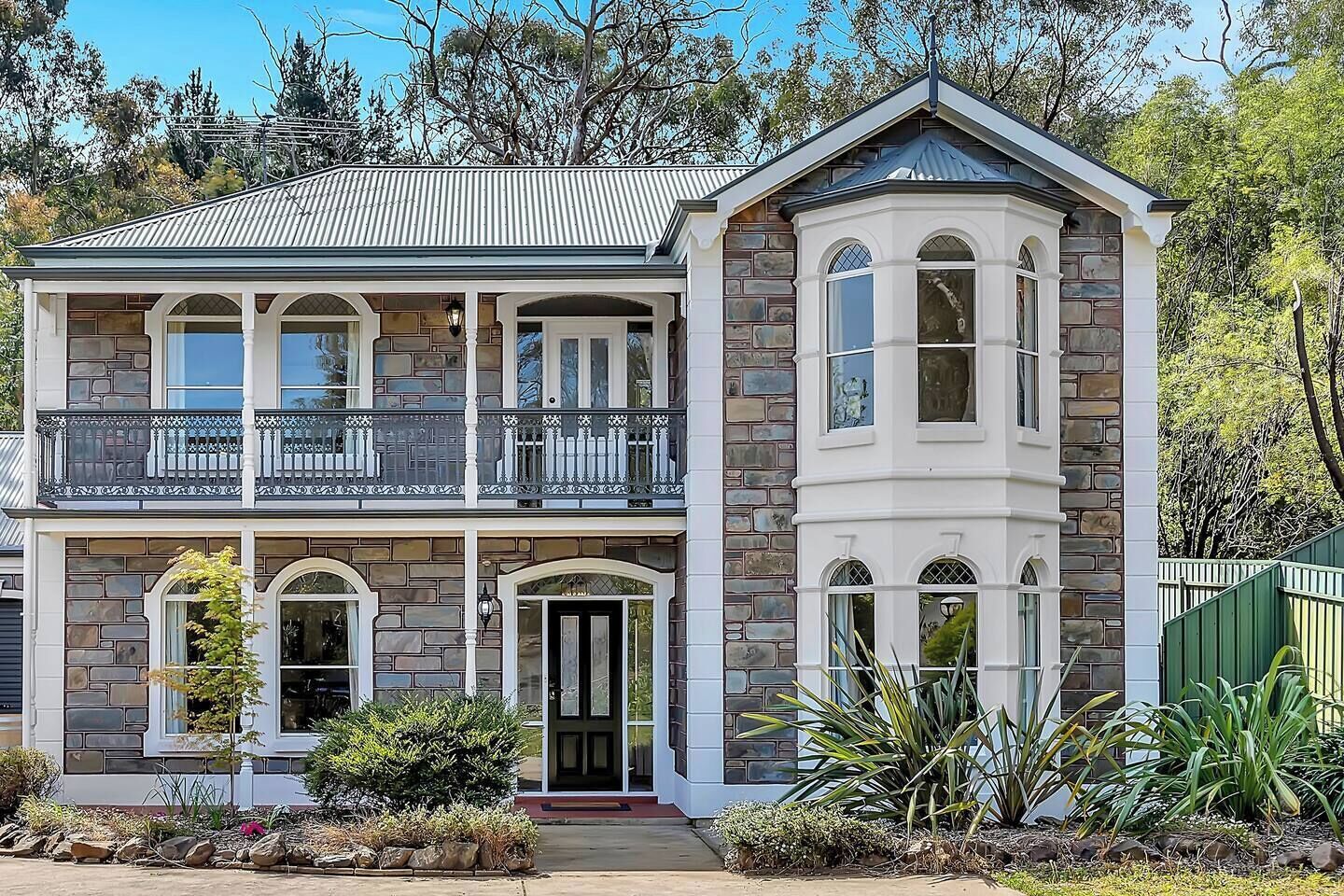 A grand stone façade with arched windows and an iron balcony captures timeless architecture surrounded by mature greenery.