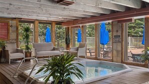 A covered outdoor pool area with lounge chairs and umbrellas, surrounded by wooden deck and glass walls. - Premier 1BR + Den w/ Pool & Hot Tub Access (Keystone)
