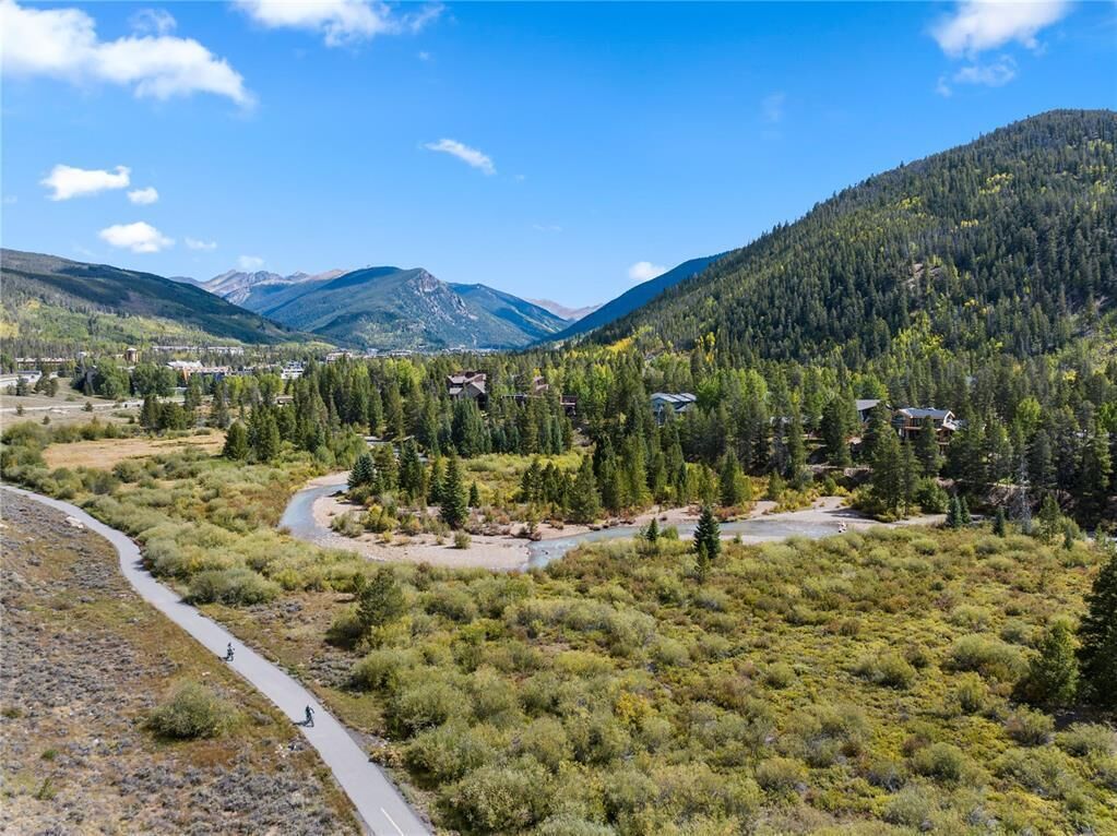 A mountainous landscape with a winding road, dense forest, and scattered buildings.