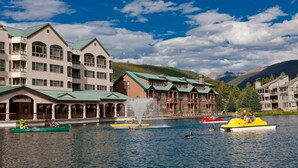A lakeside hotel with multiple buildings, a fountain, and boats on the water. - Premier 1BR + Den w/ Pool & Hot Tub Access (Keystone)