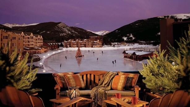 A ski resort with a large ice rink, snow-covered mountains, and a cozy seating area with a view of the rink. - Premier 1BR + Den w/ Pool & Hot Tub Access (Keystone)