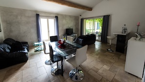 A modern living room with a glass-top dining table, black leather sofa, and a TV. - Maison l'Oustalette de Mau-bé with Pool in the Luberon (Maubec)