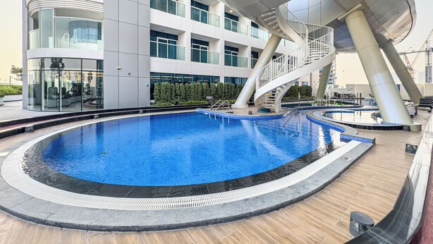 A modern building with a pool area, including a circular pool and a spiral staircase. - Superhost Spacious 1BR Arjan (Dubai)
