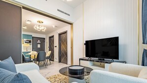 A modern living room with a sofa, a coffee table, a TV, and a dining area with chairs and a table. - Superhost Spacious 1BR Arjan (Dubai)