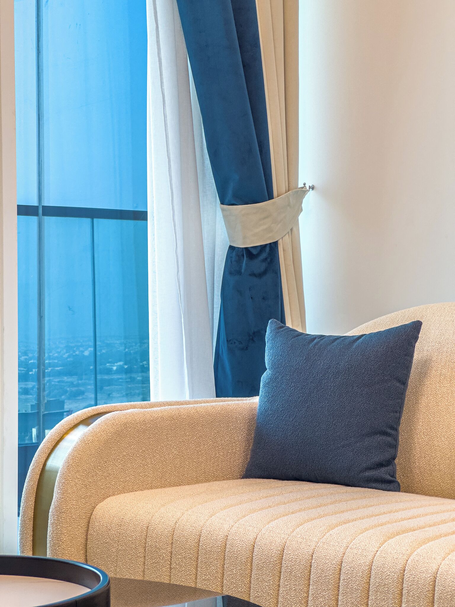 A modern living room with a large window, a sofa, and a view of the cityscape.