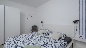 A bedroom with a bed, a chair, a nightstand, a lamp, and a wall with a blue stripe.