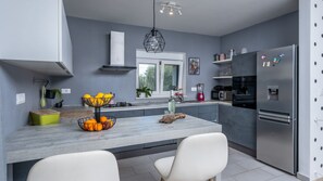 A modern kitchen with grey walls, a central island, white chairs, and stainless steel appliances.