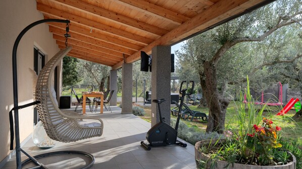 A covered outdoor area with a swing chair, exercise equipment, and a dining table.
