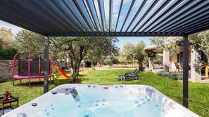 Een bubbelbad onder een pergola, een glijbaan en een terras met buitenmeubilair.