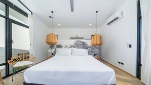 Un dormitorio con una cama grande, dos lámparas colgantes, un ventilador de techo y vistas al exterior a través de un ventanal.