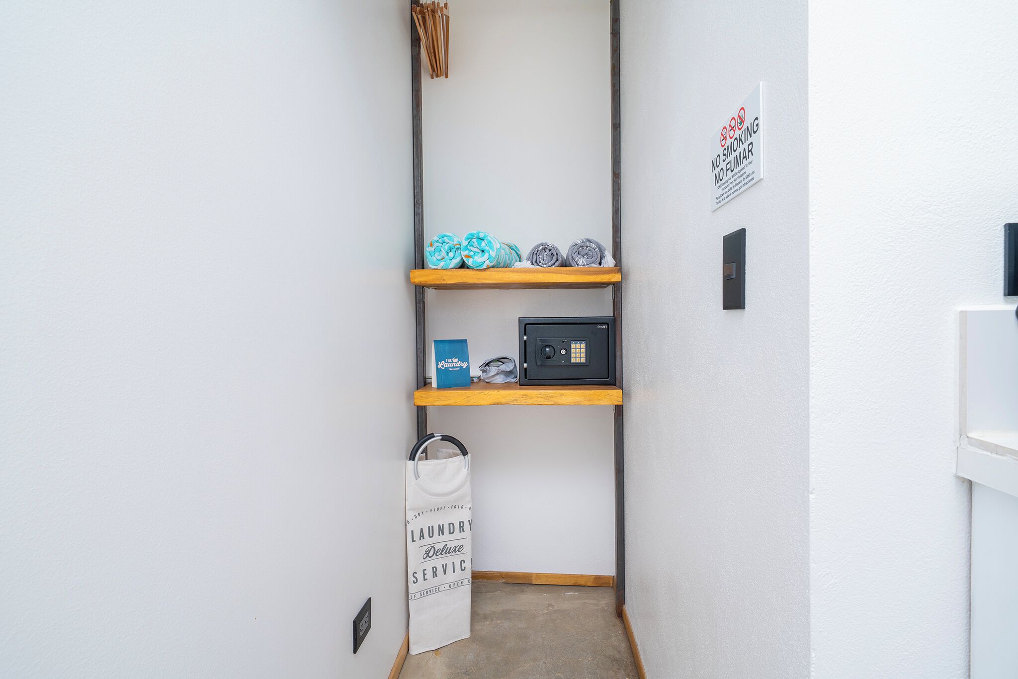 A narrow hallway with a wooden shelf holding rolled towels and a microwave. A white tote bag hangs on the wall, and a sign indicates no smoking.