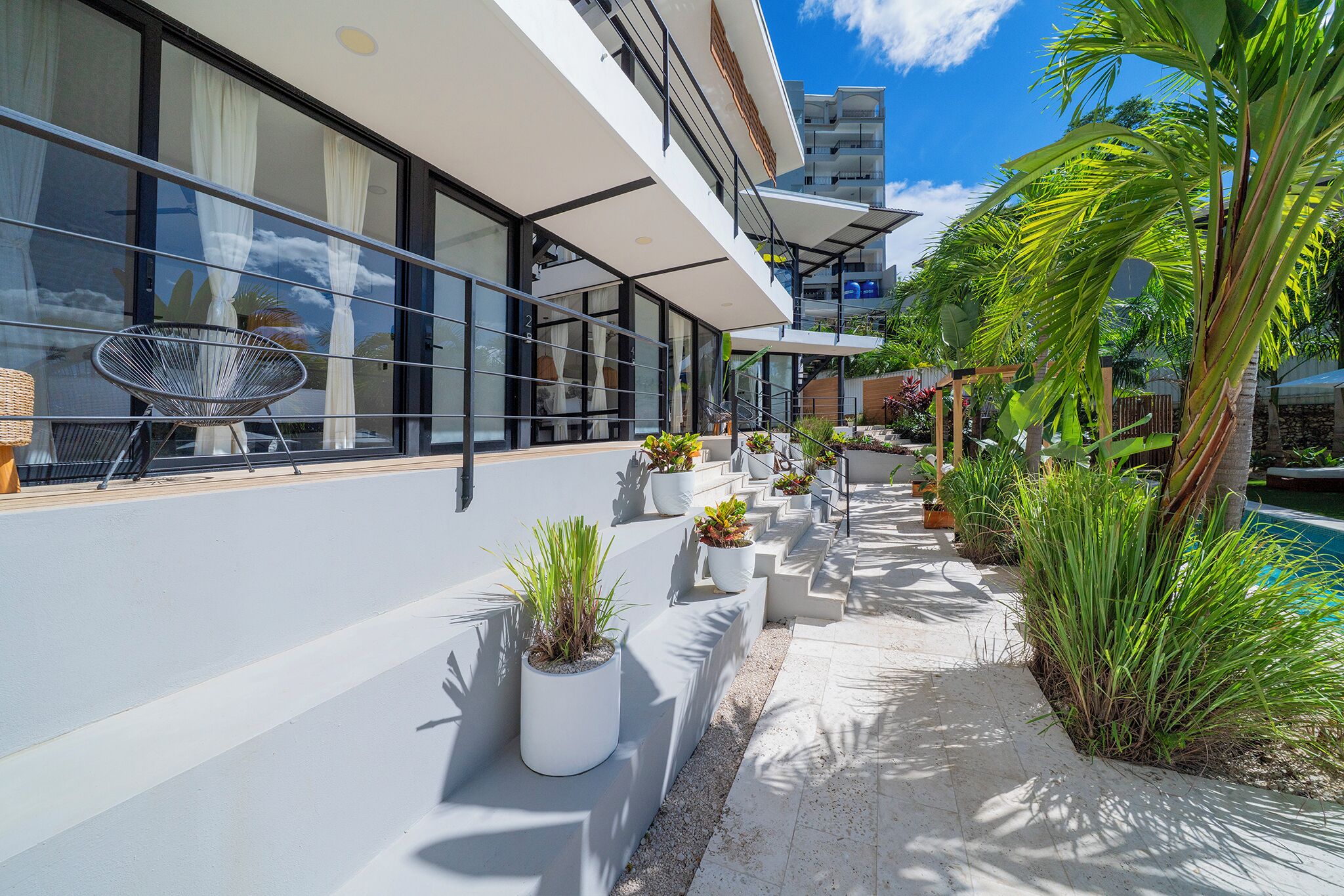 Un hotel moderno con balcón, plantas en macetas y zona de piscina.