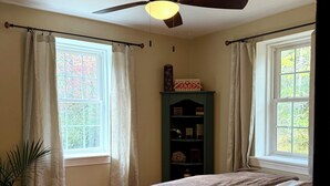 Camera da letto con un letto, una ventola a soffitto, una finestra con tende, un comodino e una lampada.