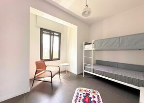 Ein Zimmer mit einem Etagenbett, einem Stuhl, einem kleinen Tisch und einem Fenster.