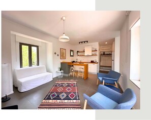 Ein modernes Wohnzimmer mit einer Couch, zwei blauen Sesseln, einem gemusterten Teppich, einer Küchenzeile mit Bar und einem Esstisch.