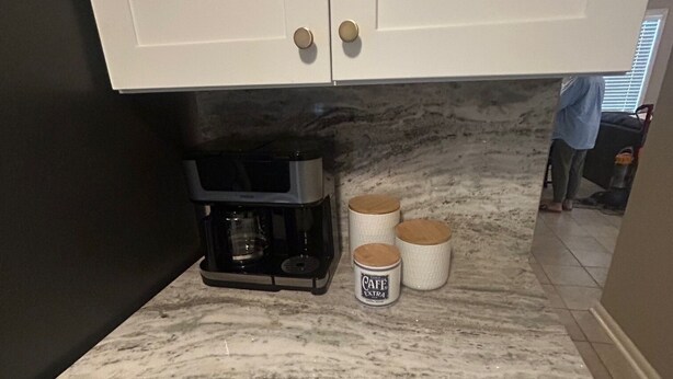 Et køkken med hvide skabe, en marmorbordplade og en kaffemaskine.