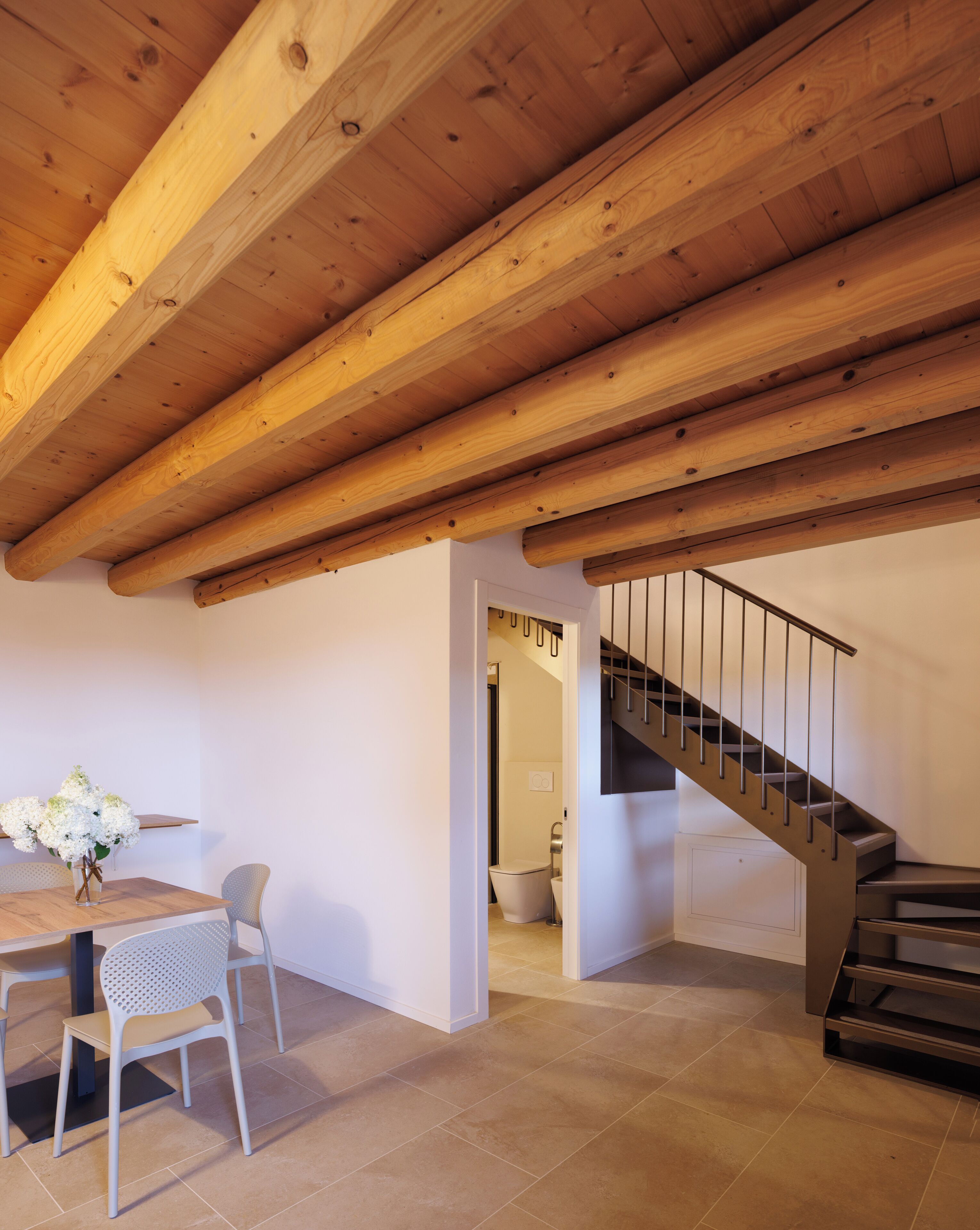 Una habitación amplia con techo de madera, un comedor con mesa y sillas, y una escalera que conduce a otro nivel.