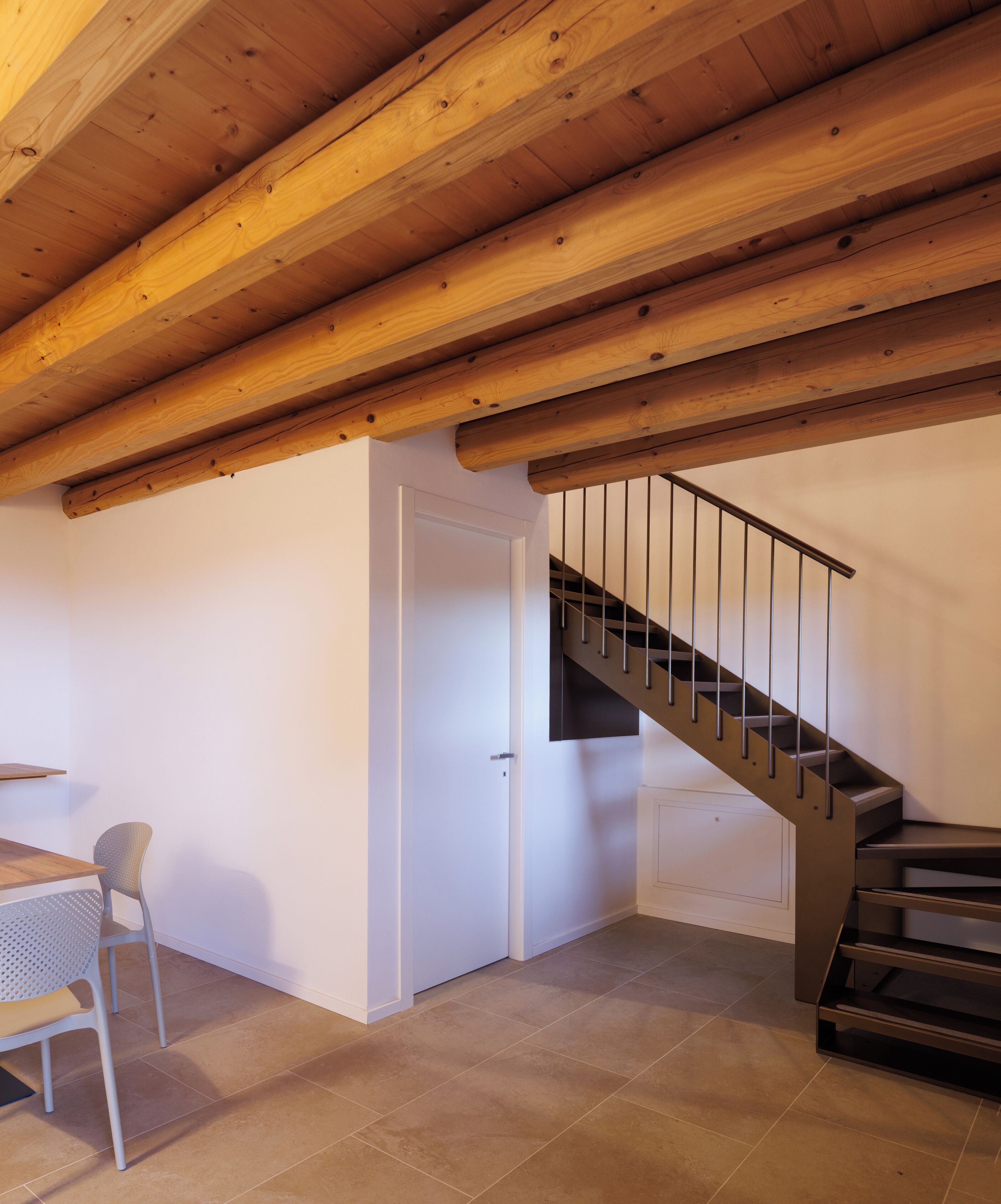 Une pièce avec un plafond en bois, un escalier, une porte blanche et une table avec une chaise.