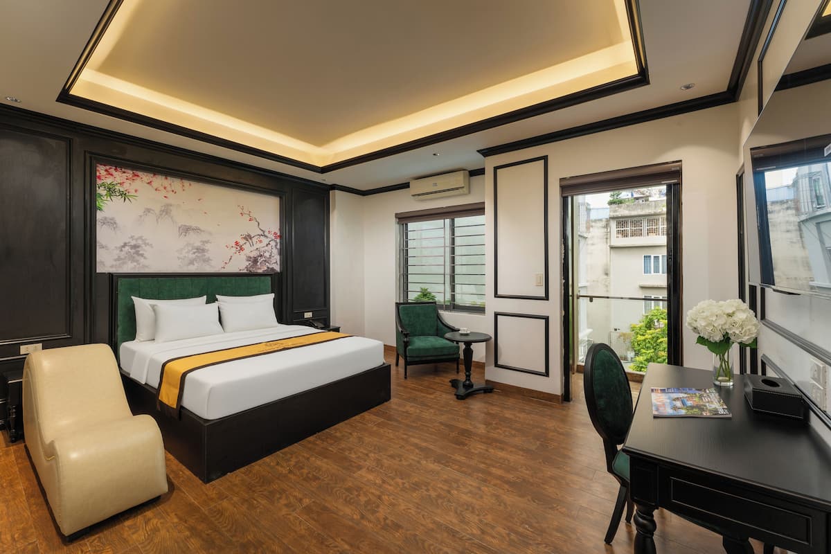 A hotel room with a bed, a desk, a chair, a small table, and a window.