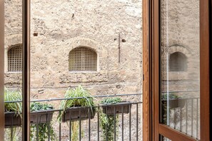 Vista de un edificio de piedra con ventanas arqueadas y un balcón con plantas en macetas.