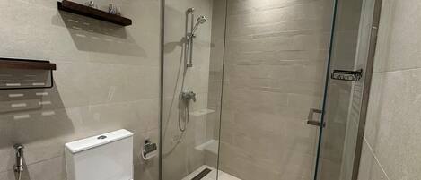 A modern bathroom with a glass-enclosed shower, a toilet, and a shelf with toiletries.