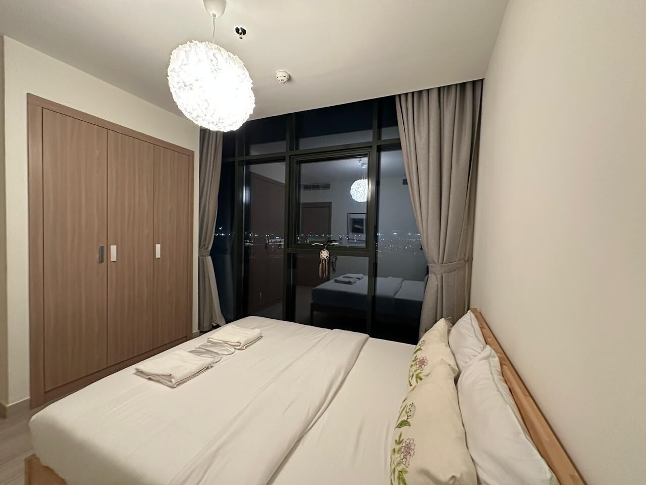 Hotellihuone, jossa on sänky, vaatekaappi, työpöytä ja näkymä kaupunkiin yöllä.