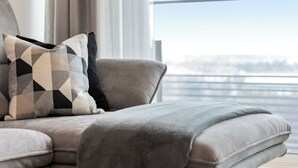 A modern living room with a sectional sofa, a coffee table, and a view of a cityscape through large windows. - Penthouse Apartment with Rooftop Pool (Vienna)
