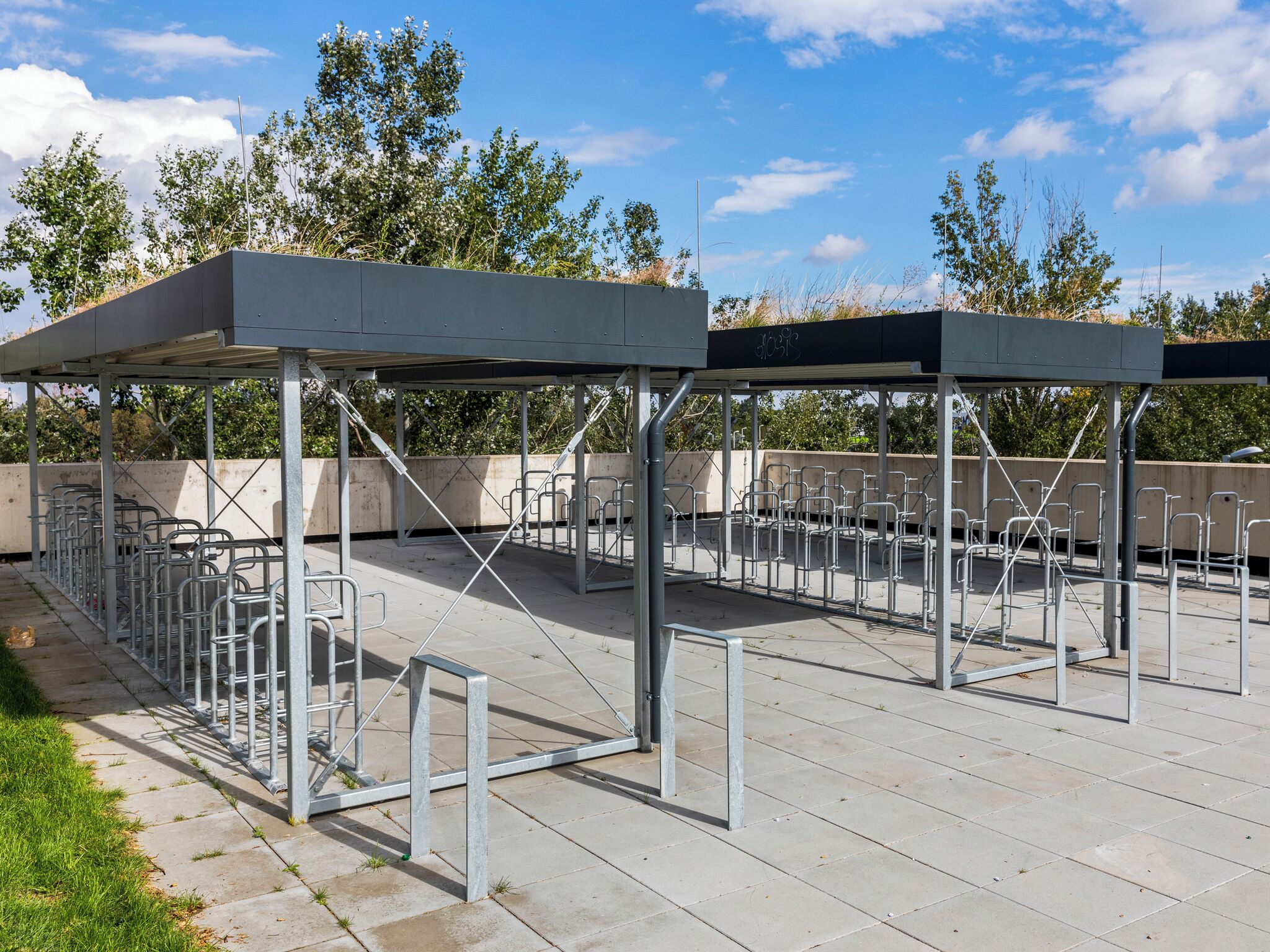 Un espace extérieur aménagé avec des chaises et des tables en métal, une partie abritée et une vue sur les arbres et le ciel.
