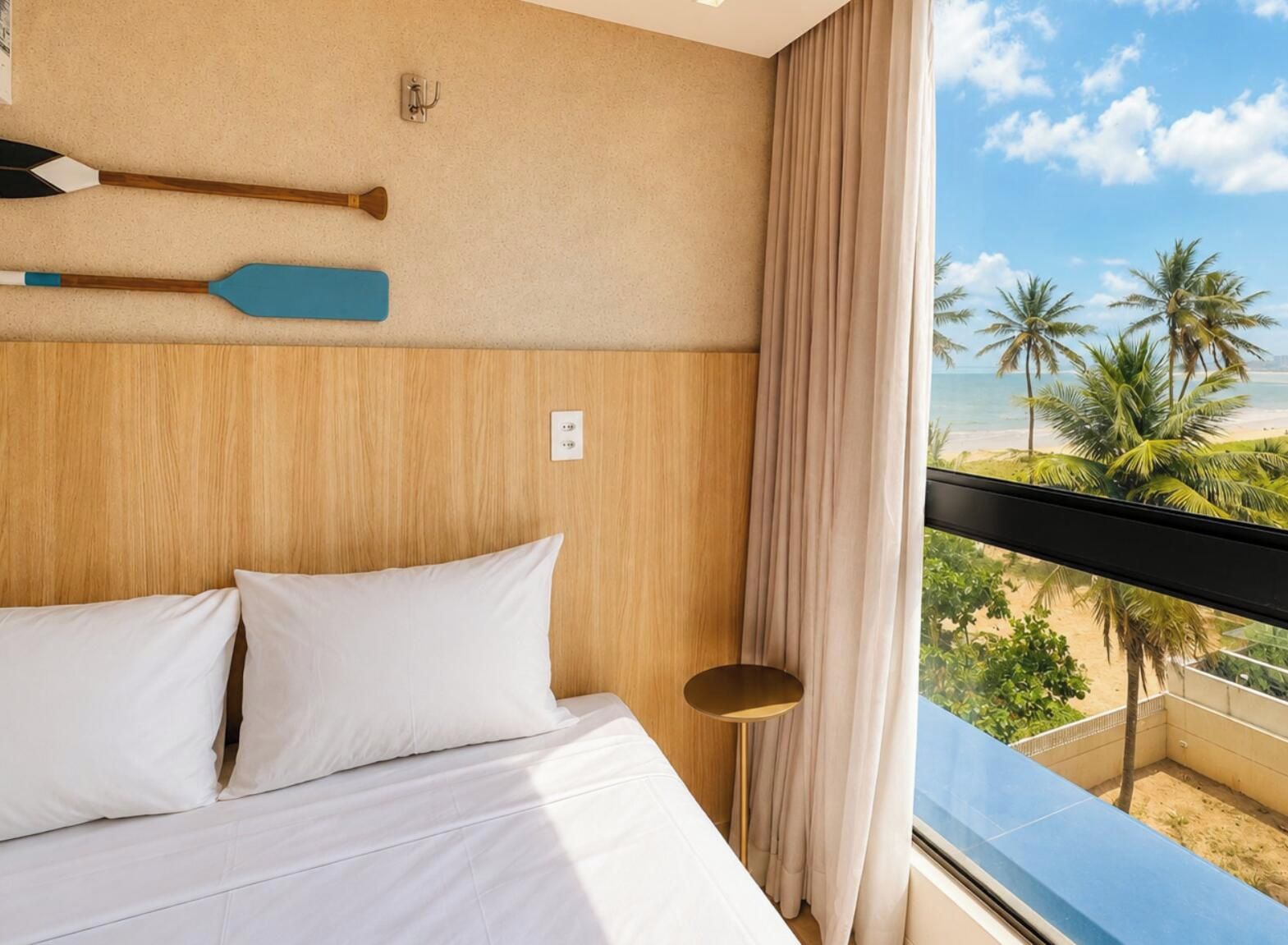 Habitación de hotel con una cama, vista a la playa y una tabla de remo fijada a la pared.