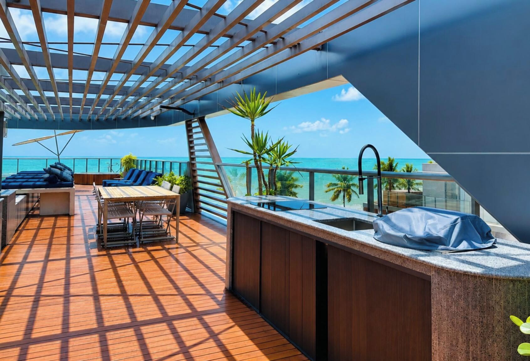 A sunlit outdoor deck with a dining area, bar, and lounge chairs overlooking the sea.