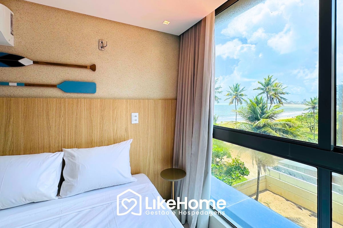 Ein Hotelzimmer mit Bett, Blick auf den Strand und einem Vorhangfenster.