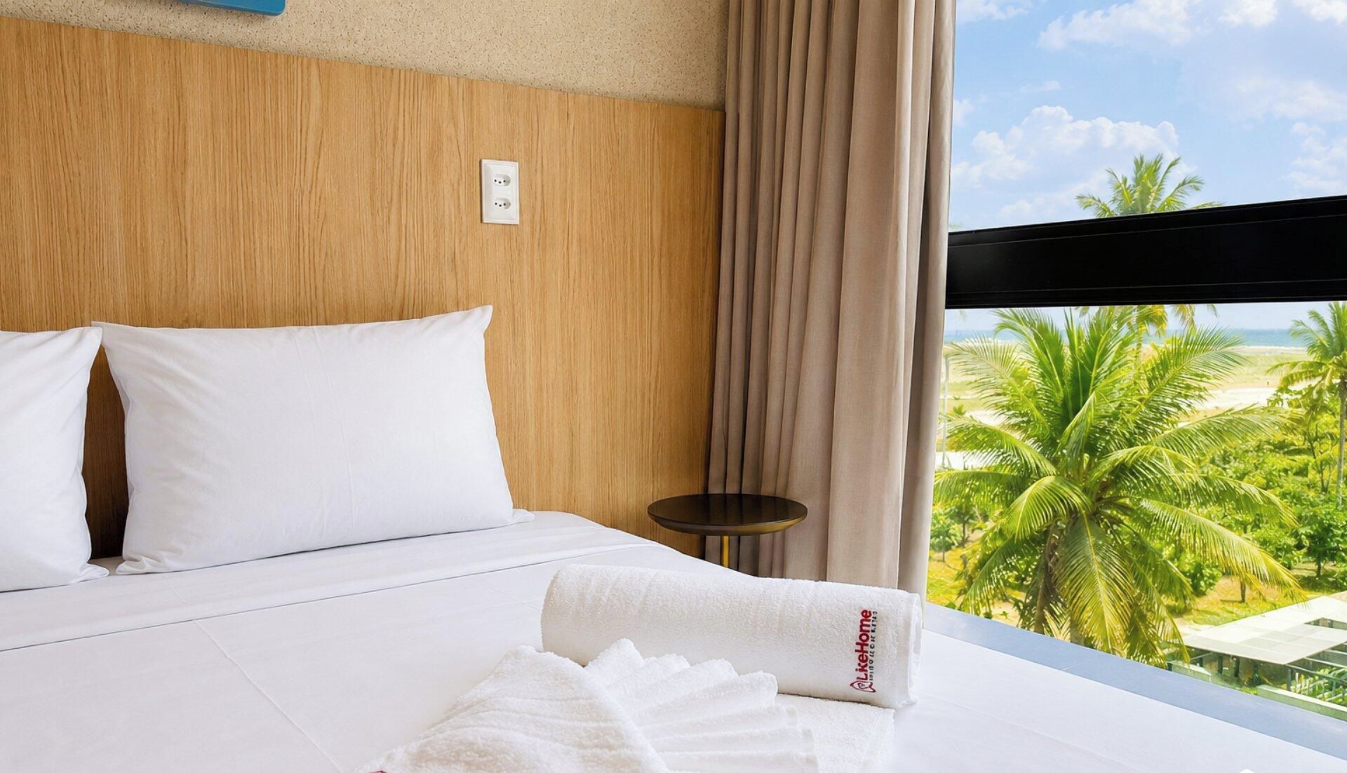 Una camera d'albergo con un letto, un tavolino, una finestra vista palme e spiaggia.