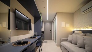 A modern hotel room with a flat-screen TV, a dining area with a table and chairs, a sofa, and an air conditioning unit. - Setai Aquamaris - LikeHome Hospedagens (João Pessoa)
