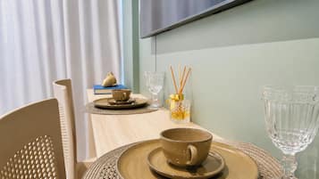 Una mesa de comedor preparada con una taza, platillo, y cristalería, con un jarrón decorativo y un difusor de aroma en el fondo.