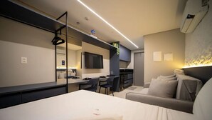 A modern hotel room with a bed, a desk, a sofa, a TV, and a kitchen area. - Setai Aquamaris - LikeHome Hospedagens (João Pessoa)