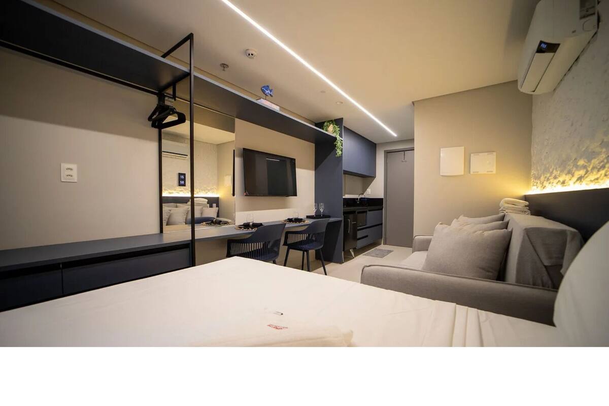 Ein modernes Hotelzimmer mit Bett, Schreibtisch, Sofa, Fernseher und einer Küchenzeile.