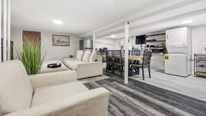 Een moderne woonkamer met een bank, een eettafel en stoelen. Er is een keuken met apparatuur en een televisie.