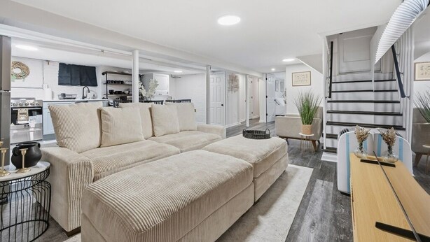 Een moderne woonkamer met een beige hoekbank, een houten salontafel en een keuken op de achtergrond.