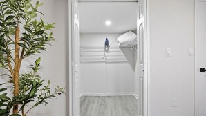 Een kamer met een bed, een witte kledingkast, een droogrek en een potplant.