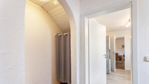 Un pasillo con piso de madera, paredes blancas y una puerta que da a una habitación con piso de madera.