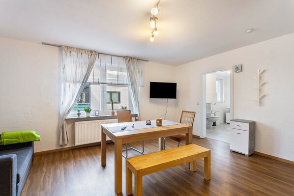 A modern, well-lit room with a wooden dining table, bench, and a flat-screen TV mounted on the wall.
