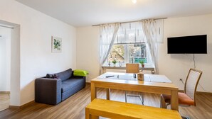 Una sala de estar moderna con un sofá, una mesa de comedor, un banco, un televisor y una ventana con cortinas.