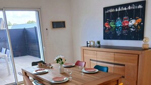 Een eetgedeelte met een houten tafel, kleurrijke stoelen en een schilderij erboven.