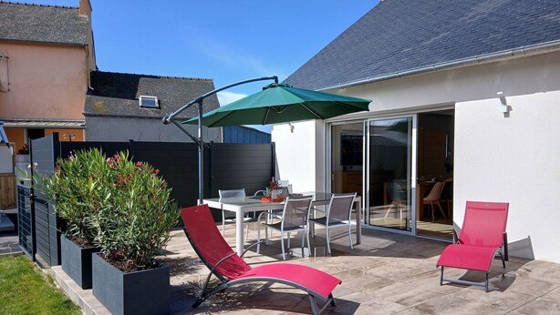 Een terras met een tafel en stoelen, een rode loungestoel en een groene parasol.
