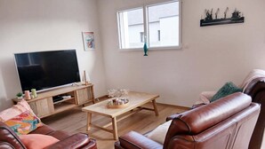 Een woonkamer met een televisie, houten meubels en uitzicht op buiten.