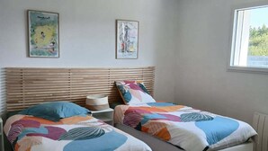 Een slaapkamer met twee eenpersoonsbedden, houten hoofdborden, een nachtkastje en twee kunstwerken aan de muur.